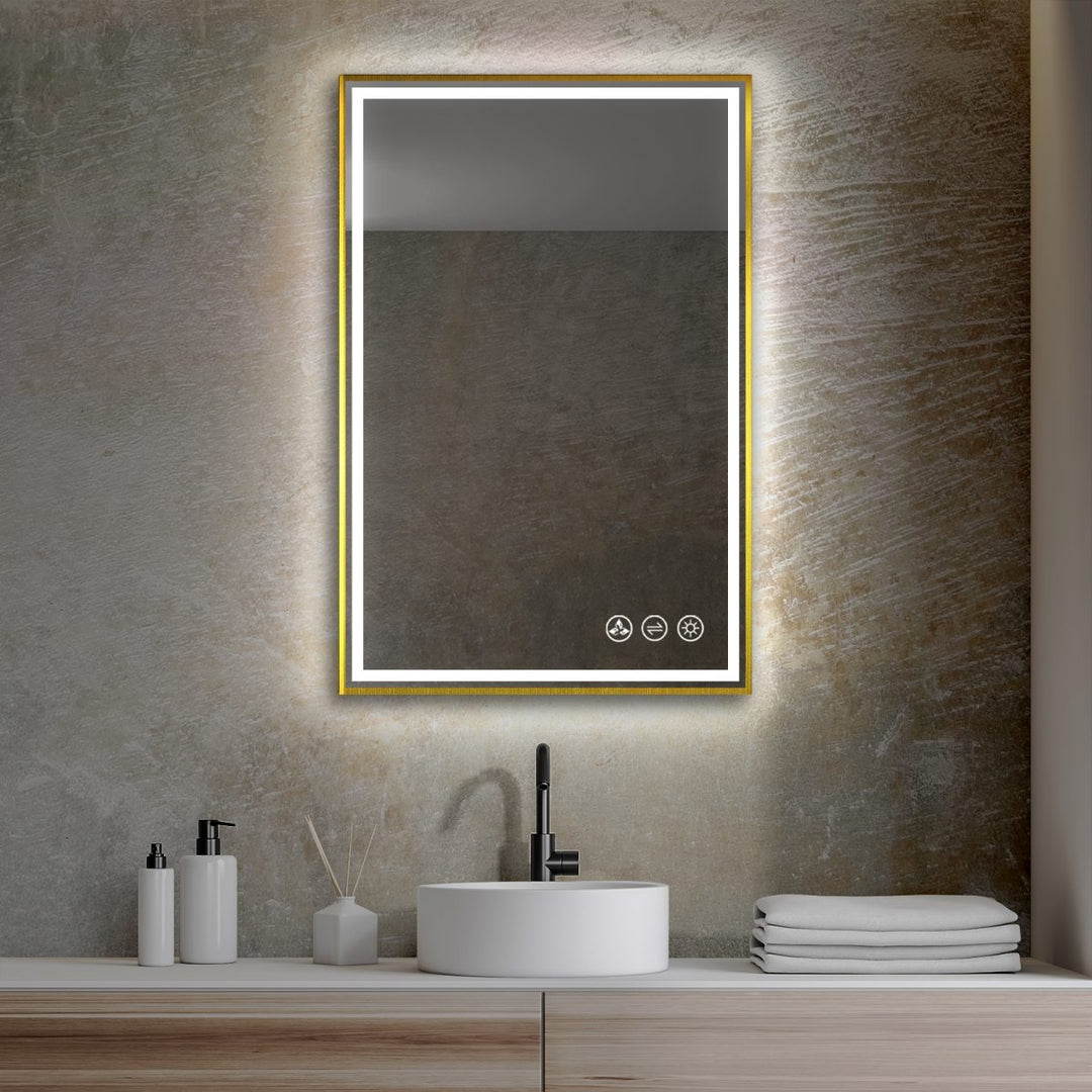 A contemporary bathroom features the Stellar 18 Inch LED Light Bathroom Mirror, framed in gold and mounted on a textured wall. Below, a round white sink with a black faucet is beautifully accented by soap dispensers, a reed diffuser, and neatly stacked towels.