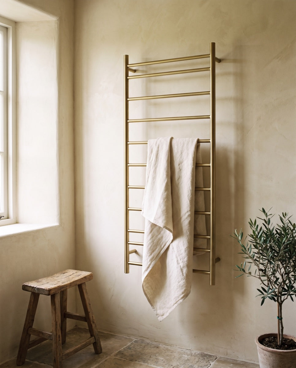 A slim heated towel warmer rail mounted on a warm cream wall in the ANVE showroom.