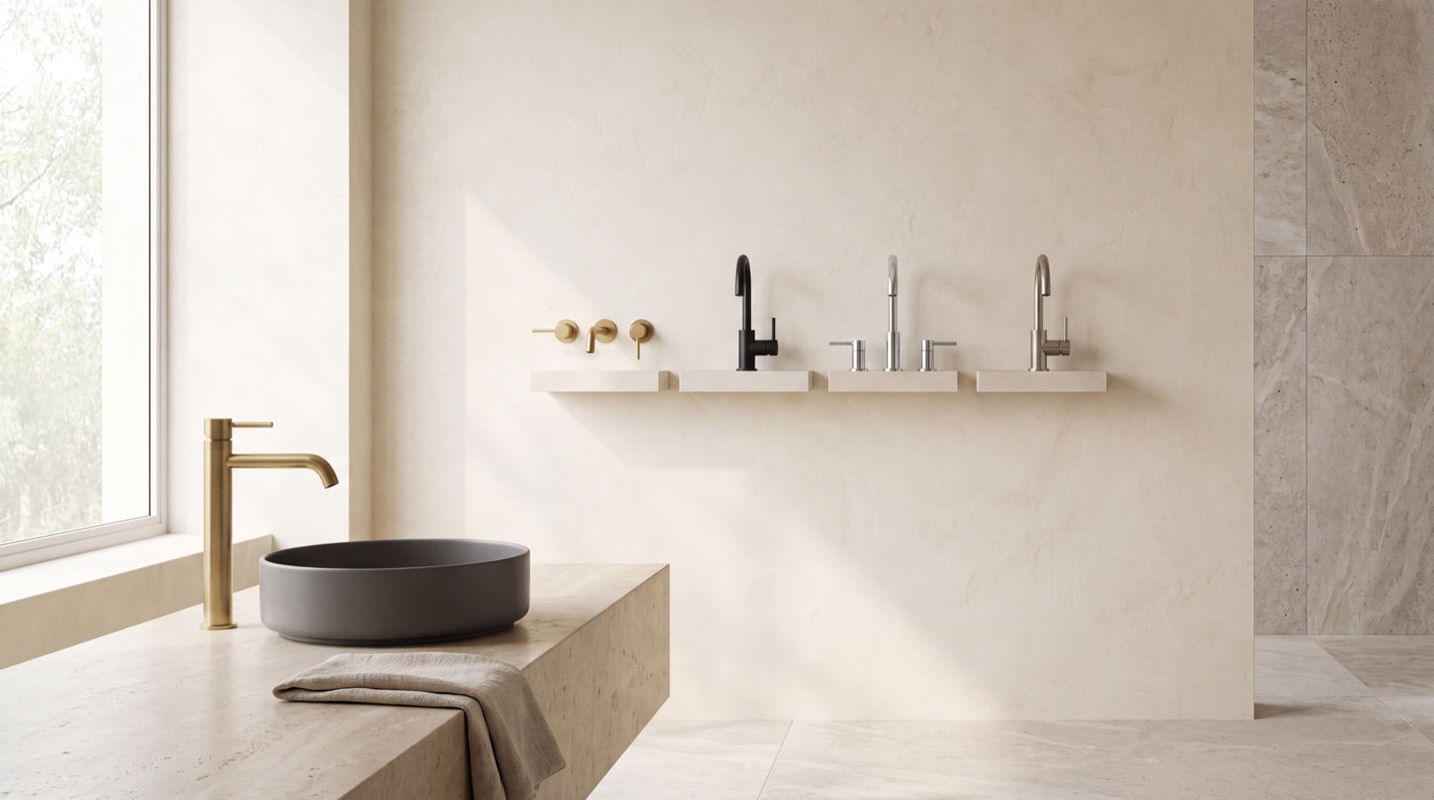 A wall display of bathroom and kitchen faucets in brushed gold, matte black, chrome and brushed nickel with a brushed-brass faucet on a stone vanity in the ANVE Paramus showroom.