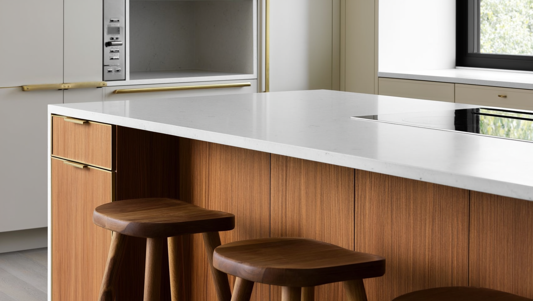 Custom kitchen island with white quartz top, warm walnut base cabinetry, integrated drawers and a microwave nook, brass hardware, and three wood counter stools