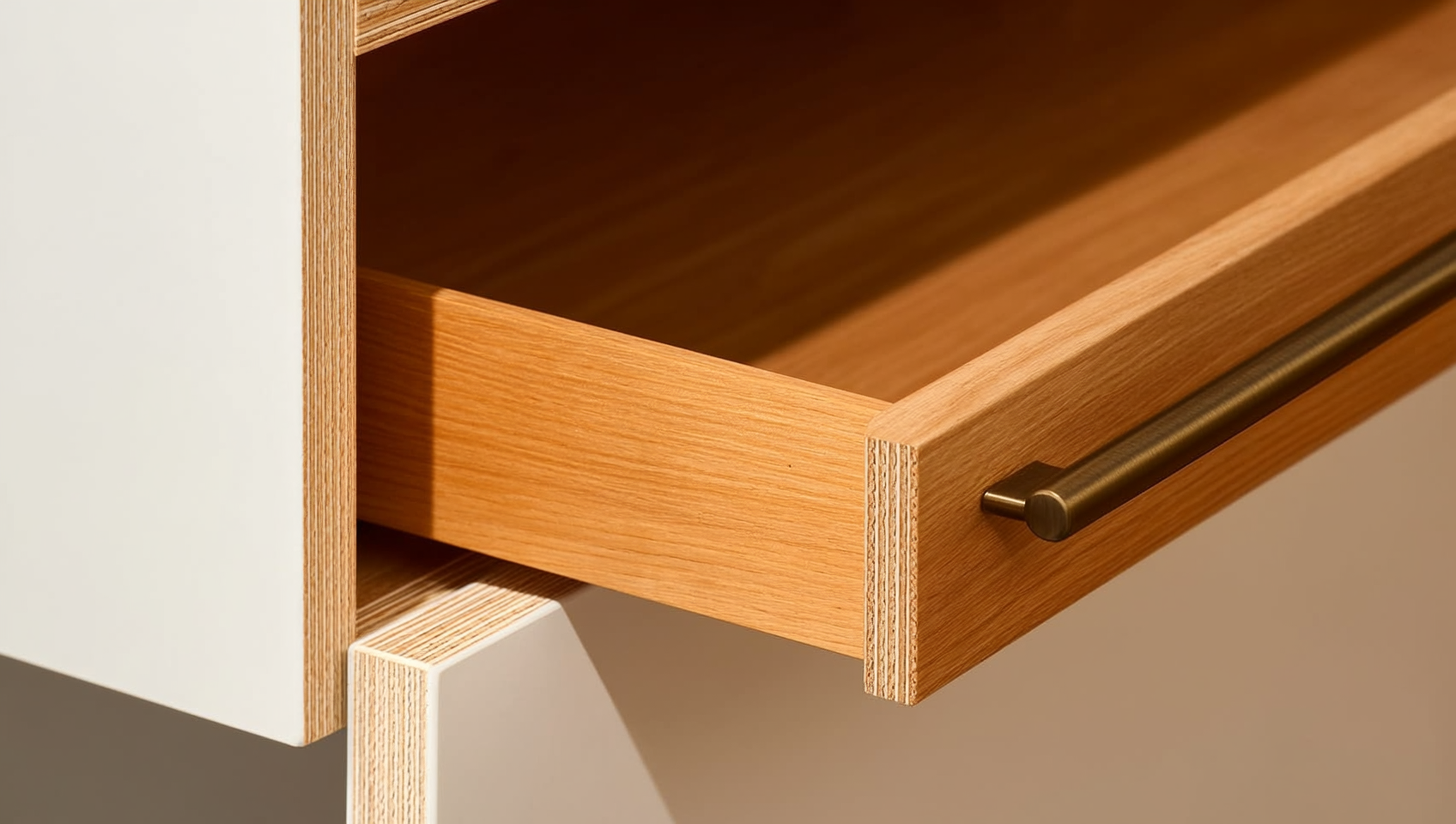 Close-up of a dovetail solid-wood kitchen drawer box on a soft-close glide with a plywood cabinet box edge and brushed-brass handle