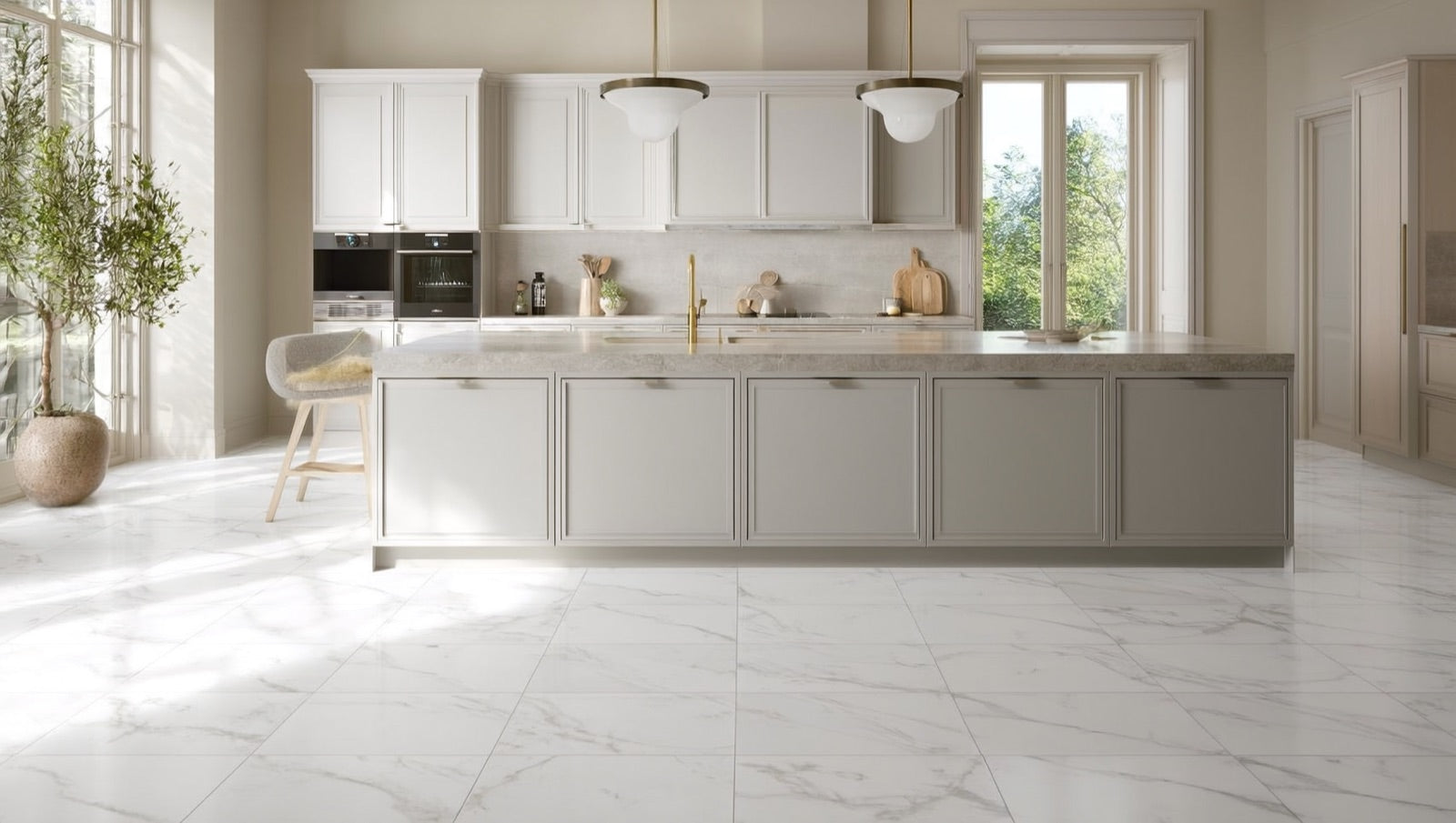 Bright kitchen floored in 24x48 marble-look matte porcelain tile in Bianco with soft grey veining, beneath pale cabinetry and a stone-topped island