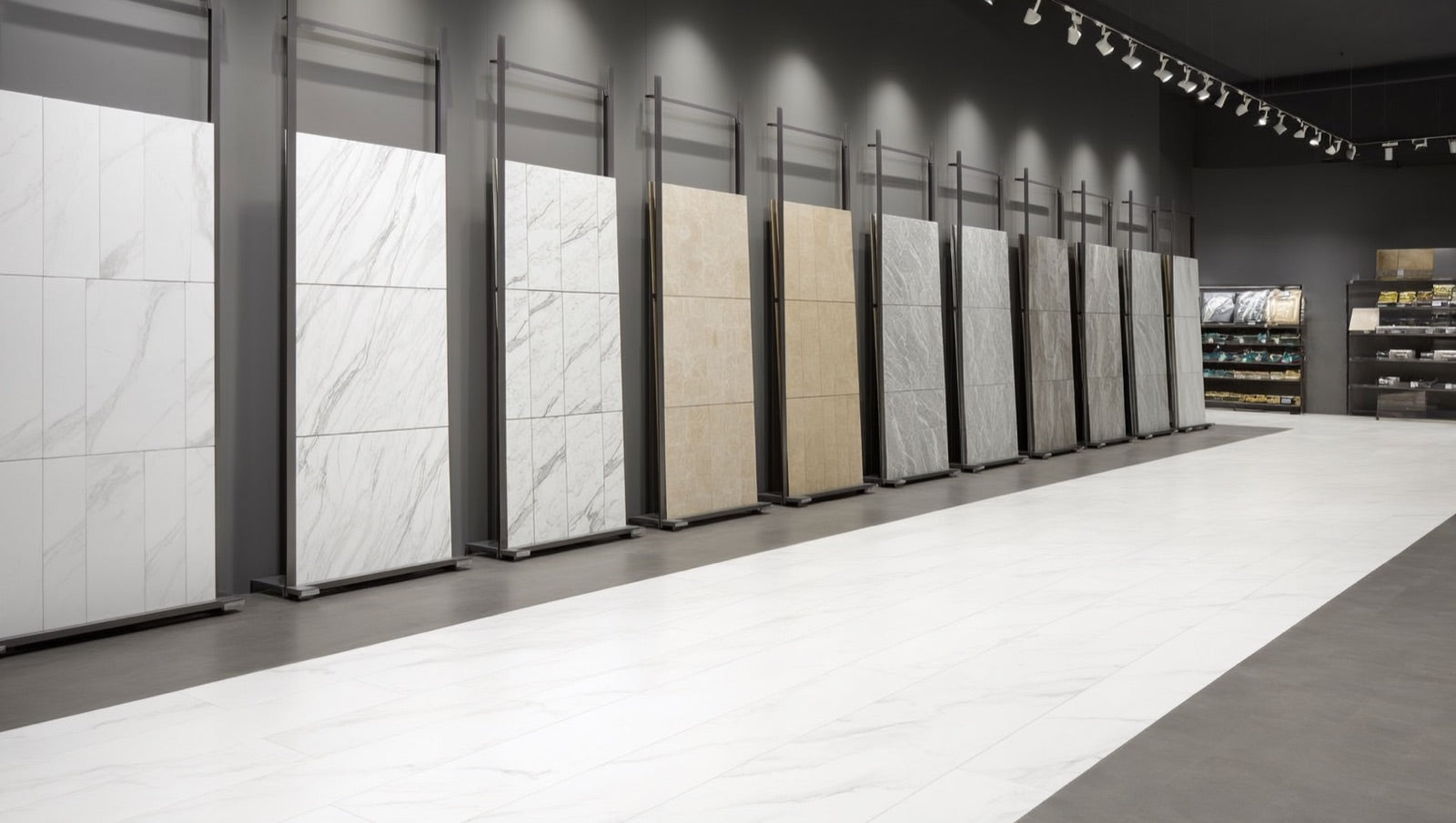 Showroom display of upright large-format porcelain tile panels in white, beige, and grey marble-look and stone-look designs, arranged in browsing racks