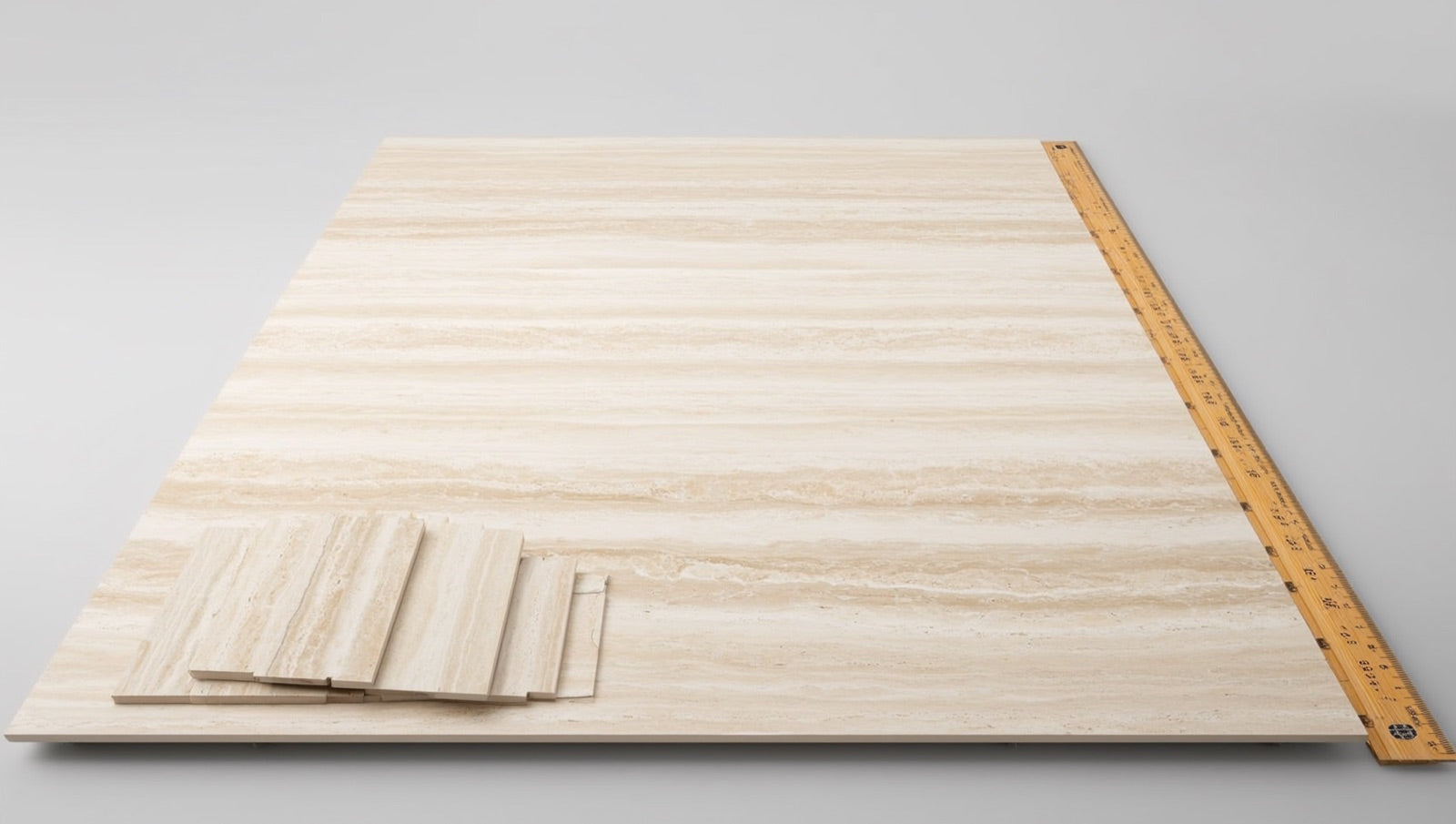 Slab planning table with a travertine-look porcelain sample laid flat beside 24x48 and 12x24 companion pieces, a hexagon mosaic sheet, and a folding rule marking an island end dimension.