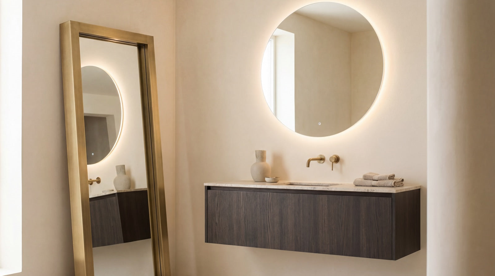 A round LED back-lit bathroom mirror glowing above a floating wood vanity beside a tall brushed-brass framed mirror in the ANVE Paramus, New Jersey showroom.