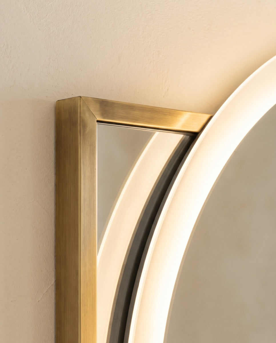 A detail of a slim brushed-brass mirror frame meeting a softly glowing LED back-lit mirror edge.