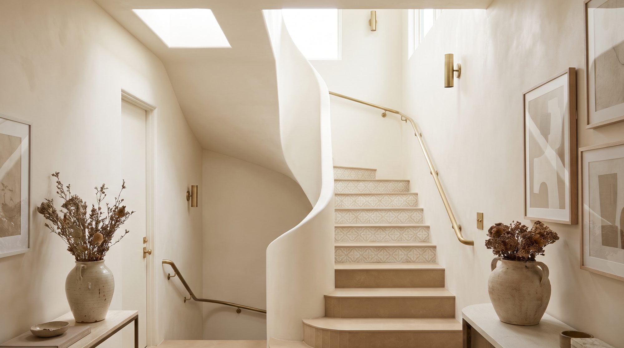 A staircase with warm matte porcelain treads, decorative patterned tile risers, and a soft brass stair rail against a cream plaster wall in the ANVE style.