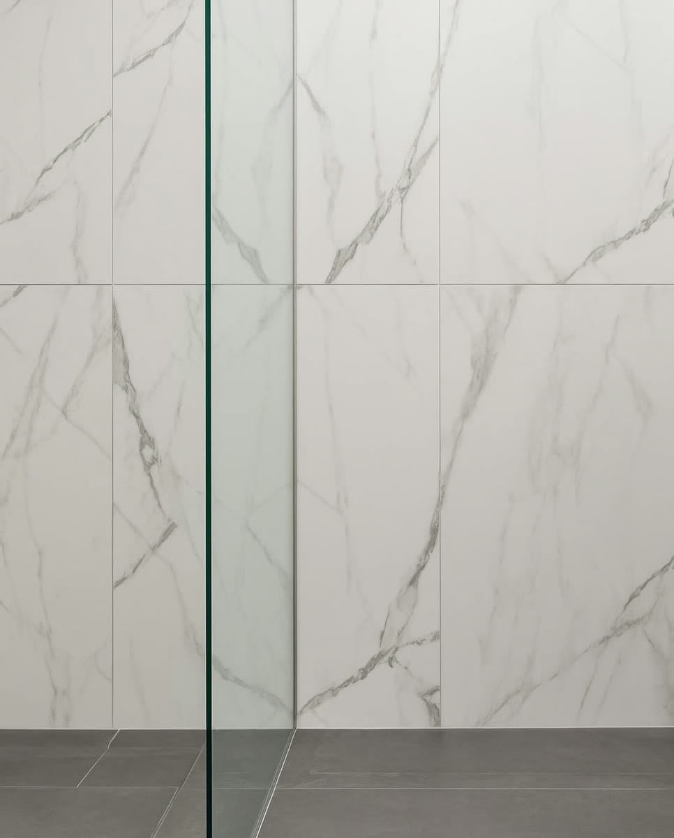 A bathroom corner where marble-look porcelain shower wall tile meets matte grey porcelain floor tile in the ANVE showroom.