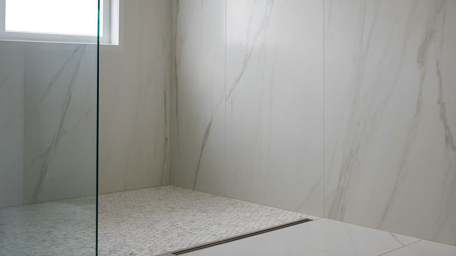 A walk-in shower display with marble-look porcelain slab walls and a matte hexagon mosaic shower pan in the ANVE Paramus, New Jersey showroom.