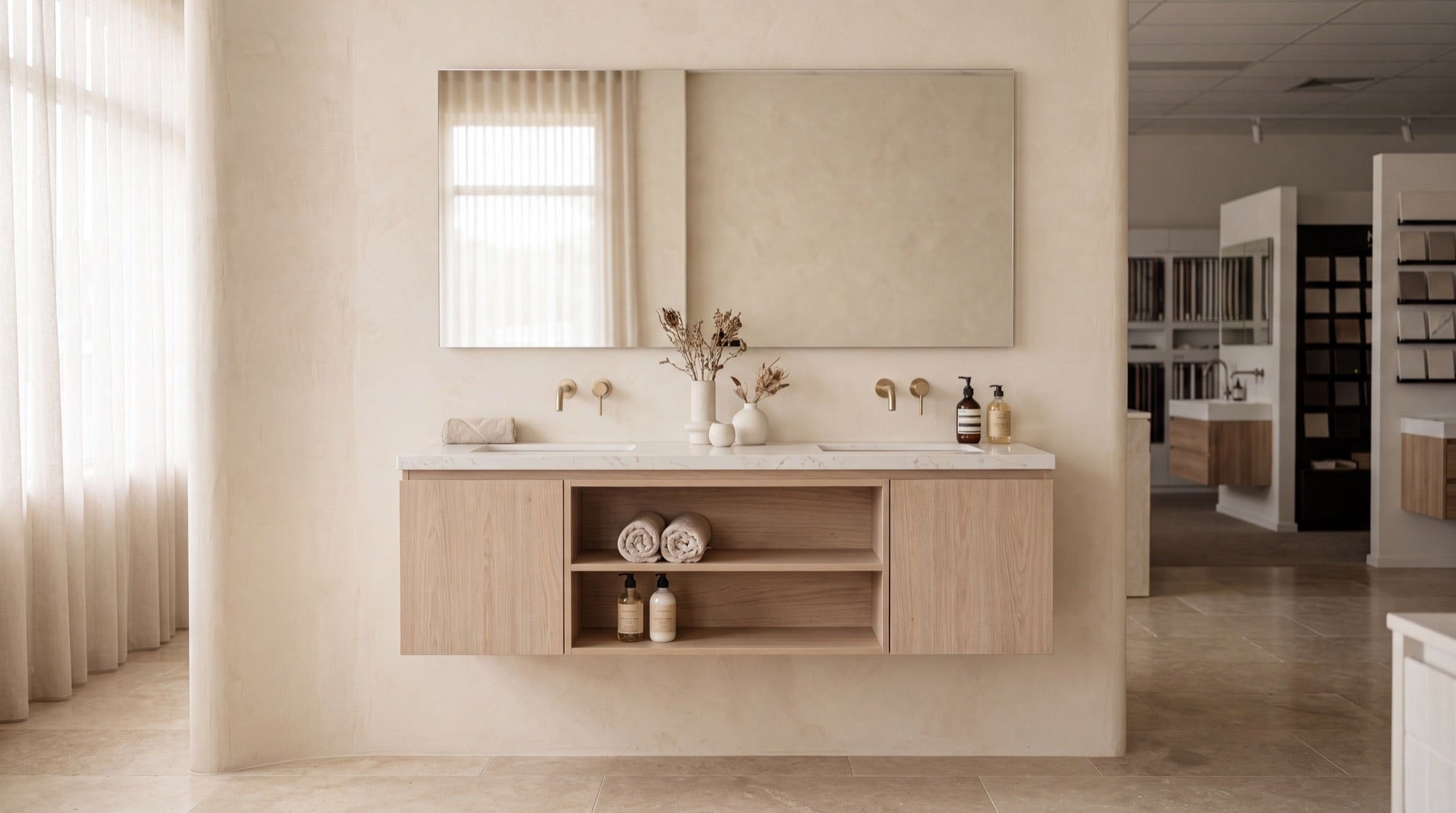 A floating white-oak double bathroom vanity with a honed stone top and brushed-brass wall faucets in the ANVE Paramus showroom.