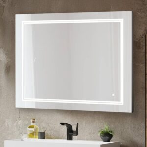 The Soho 36 Inch x 30 Inch LED Lighted Bathroom Mirror hangs above a white sink with a black faucet. On the counter are a bottle, glass, and small potted plant, all set against a textured wall.