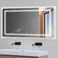 A Soho 60 Inch x 30 Inch LED Lighted Bathroom Mirror hangs above a modern white sink with two black wall-mounted faucets; the backlit mirror reflects a window and part of a gray wall.