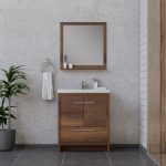 Modern bathroom with a wooden vanity, square mirror, and white sink. A towel hangs on a ring, toiletries sit on the counter, and a green plant is on the left, against a concrete wall and tiled floor.