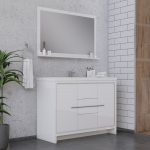 Modern bathroom vanity with a large mirror, white cabinet, sink, and faucet. A towel hangs on a ring to the left, with a potted plant nearby. The walls are concrete and white tile, and the floor is dark gray.