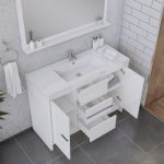 A modern white bathroom vanity with open drawers and cabinet doors, revealing neatly folded towels and toiletries. The countertop holds soap dispensers, cups, a tray, and towels. A large mirror hangs above.
