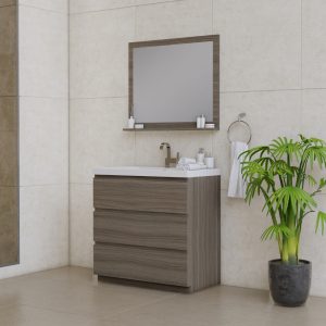 Modern bathroom with a wood vanity, white sink, and mounted mirror. There are toiletries on the vanity, a towel on a ring, and a green potted plant in the corner. The walls and floor are light-colored tiles.