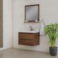 A modern bathroom with a wooden floating vanity, white sink, and matching mirror. A hand towel hangs on the wall, and a potted green plant sits on the floor beside the vanity. The walls and floor are beige tiles.