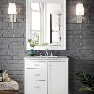 A modern bathroom features the Addison 30 inch Bathroom Vanity in Glossy White with a marble countertop, a rectangular mirror, and two white-shaded sconces. The dark gray brick wall contrasts beautifully with the light wood herringbone floor, accented by a plant and decorative items.