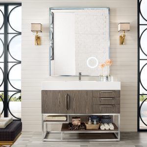 The modern bathroom showcases the Columbia 48 Single Bathroom Vanity in Ash Gray with brushed nickel fixtures. A large mirror is positioned above, flanked by circular wall lights, and open shelving allows for towel and basket storage. Circular side windows bring in light, maintaining a tranquil neutral tone.