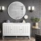 The modern bathroom showcases the Athens 60 Single Bathroom Vanity in Glossy White with a large round mirror above. Two wall-mounted lamps flank it, enhancing the dark brick walls contrast against minimalistic decor. A potted plant and toiletries rest on the countertop, overlooking a city view.