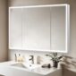 A modern bathroom features the Edge Royal 48 Inch LED Lighted Mirror 3 Door Medicine Cabinet above a white sink, with a chrome faucet, a small plant, and towels on the countertop against a beige wall.