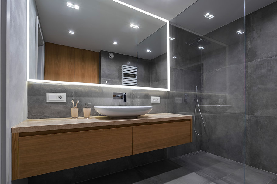 Modern bathroom with a floating wooden vanity, round sink, Edge 96 Inch LED Lighted Bathroom Mirror, gray tiled walls and floor, glass-enclosed shower, and minimal accessories on the counter.