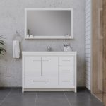 Modern bathroom with a large rectangular mirror above a white vanity with drawers and a sink. Gray tile floor, towel ring with white towel, and concrete and wood-paneled walls are visible. Minimalist décor.