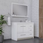 Modern bathroom with a white vanity and drawers, a large rectangular mirror, a potted plant, and a towel hanging on the wall. The background features light gray concrete and white subway tiles.