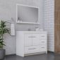 Modern bathroom with a white vanity and drawers, a large rectangular mirror, a potted plant, and a towel hanging on the wall. The background features light gray concrete and white subway tiles.