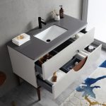 The Burano 48 inch Beige Freestanding Bathroom Vanity features a modern gray countertop, black faucet, white sink, open drawers with towels and toiletries, and a partially visible blue and beige rug.
