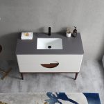 The Burano 48 inch Beige Freestanding Bathroom Vanity has a gray countertop, white rectangular sink, black faucet, soap dispenser, folded towel, and soap. It includes two drawers and wooden legs on a gray floor next to a colorful rug.