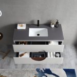 The Burano 48 inch Beige Freestanding Bathroom Vanity features a gray countertop, white sink, black faucet, soap dispenser, toothbrush holder, plus two drawers for towels and toiletries. A rug and stool are partially visible below.