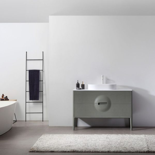 A minimalist bathroom features a 48 Advento Olive Green freestanding vanity with a sleek round basin and modern tap. A ladder-style towel rack holds a dark towel, while a white bathtub is visible. The decor is simple, with neutral tones and a gray rug completing the serene space.