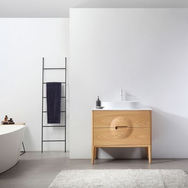 A minimalist bathroom features a 36 Advento Whitewash Oak Vanity with circular handles, paired with a white countertop and soap dispenser. A black ladder towel rack holds a dark towel beside the sleek white bathtub on the gray floor.