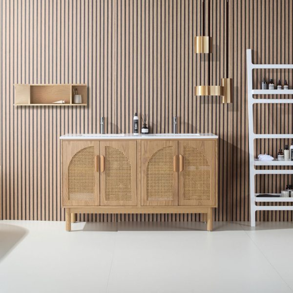 A modern bathroom includes the Nara 60 inch Freestanding Bathroom Vanity in Pecan Oak with woven cane cabinet doors, a wooden slat wall, gold pendant lights, a white shelving unit for toiletries, and a small wooden wall shelf.