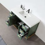 The Winchester 48 Forest Green Freestanding Bathroom Vanity includes a white countertop with an integrated sink. The green cabinet features open drawers for towels and various items. A soap dispenser and dish sit by the black faucet, complementing the vanity above gray tiled floors.