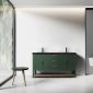 A modern bathroom features the Winchester 60 inch Forest Green Freestanding Bathroom Vanity with a black countertop and dual sinks. A wooden stool sits by a large window showcasing lush greenery, while a toilet is seen in the adjacent room against white walls.