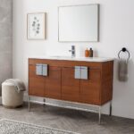 Modern bathroom with a Shawbridge 48 inch Modern Bathroom Vanity With Sink, silver handles, a rectangular mirror, two bottles on the counter, a towel on a black ring, a botanical print, and a textured stool on herringbone tile.