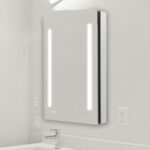 The Signature Royale 24"x36" Right Sided LED Lighted Mirror Medicine Cabinet features two vertical LED strips, a digital clock, and touch controls, perfect for mounting above a white countertop with sink and faucet.
