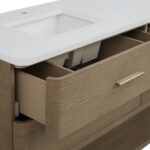 The Lucian 72 inch Double Bathroom Vanity adds a modern flair with its textured horizontal wood grain and sleek gold handles. A white countertop featuring a sink tops the vanity, and one drawer opens to display neatly organized storage compartments.