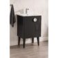 The Venezian 24 inch Bathroom Vanity With Sink in black features tapered legs, a white sink, and a sleek faucet, complemented by a gray towel. White marble tile walls and wood-look floor tiles create a stylish bathroom backdrop.