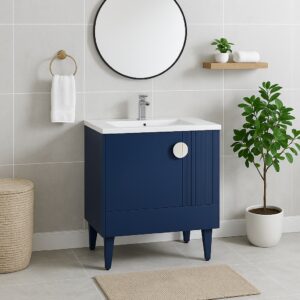 A modern bathroom featuring a Venezian 30 inch Bathroom Vanity With Sink, white countertop, round mirror, wall towel shelf, gold hand towel ring, potted plant, woven basket, and beige floor mat on light gray tiled walls and floor.