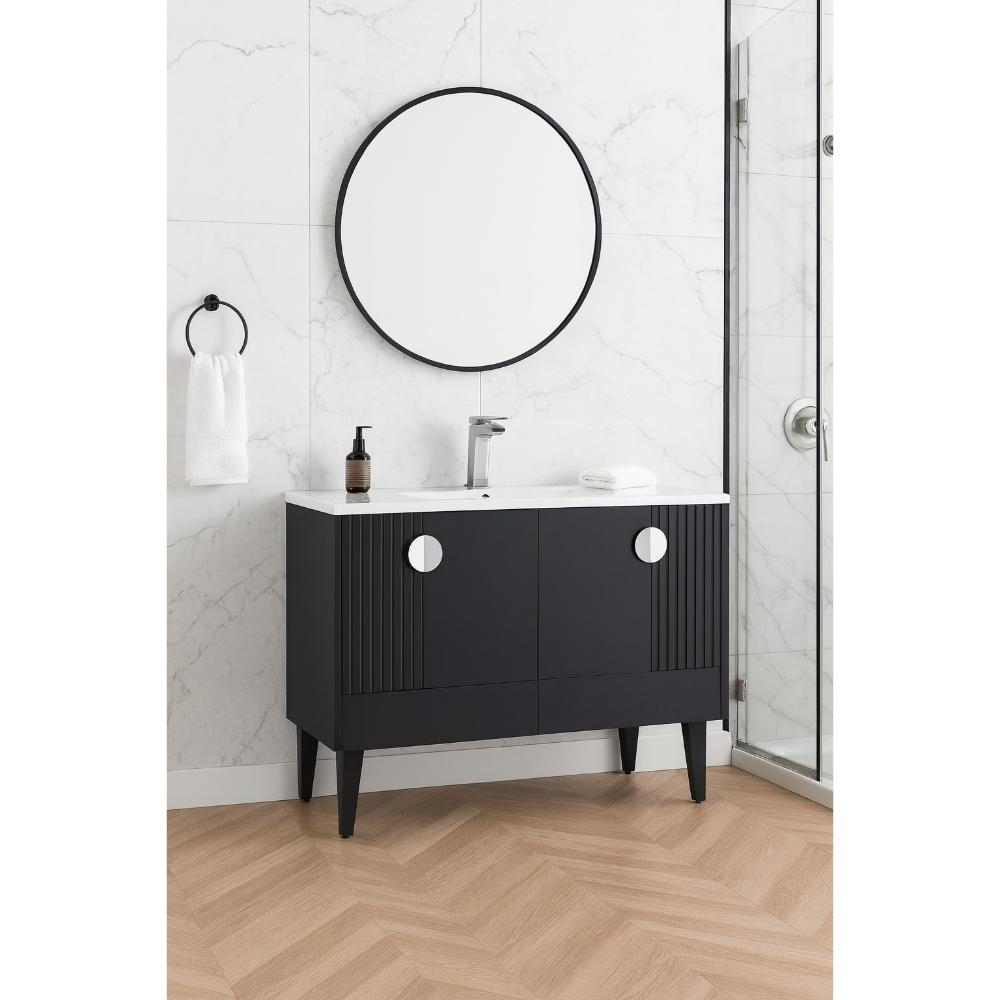 The Venezian 48 inch Bathroom Vanity with a black cabinet, white countertop, and chrome faucet sits below a round mirror on a white marble wall. A towel ring with a white towel and glass shower enclosure are also visible.