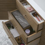 Three open wooden drawers in the Linear 72 inch Single Bathroom Vanity Cabinet reveal neatly organized items—makeup brushes, a patterned box, cosmetics, jewelry, and toiletries—set against a white hexagonal tile floor.