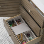An open drawer with dividers in the Linear 72 inch Single Bathroom Vanity Cabinet holds jewelry—like a pearl necklace and rings—makeup, and small containers, set against white hexagonal tile flooring.