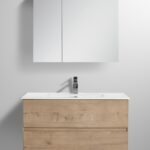 The Assisi 30 inch Wall Mounted Bathroom Vanity With Sink showcases a minimalist design with light wood and two drawers, topped with a sleek white rectangular sink and modern chrome faucet. A mirrored cabinet complements its clean lines on the wall.
