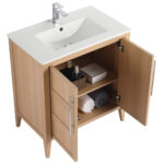 The Leafside 30 Inch Bathroom Vanity With Sink includes a white ceramic basin, modern faucet, and two open wooden cabinet doors with sleek metal handles, revealing storage shelves for rolled towels, toiletries, a small basket, and a box.