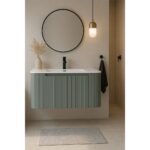 The contemporary bathroom showcases a Caskvalley 30 Inch Wall Mounted Bathroom Vanity with Sink, finished in green and topped with a sleek white sink. A round mirror adds elegance above, accompanied by a vase of dried grasses. A small pendant light enhances the setting, while a gray rug graces the tiled floor.