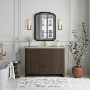 A chic bathroom showcases white paneled walls and a Gracyn 48 inch Bathroom Vanity with a marble countertop, paired with a large arched mirror. Brass sconces border the mirror. A potted plant and rug add warmth, and a freestanding bathtub is partially visible.