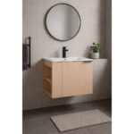 This modern bathroom showcases the Elmridge 24 Wall Mounted Bathroom Vanity with a sink, a black faucet, and a round mirror. A potted plant sits on the ledge, complemented by a dark towel on a black rack and a beige mat on dark tiles, highlighting its minimalist style.